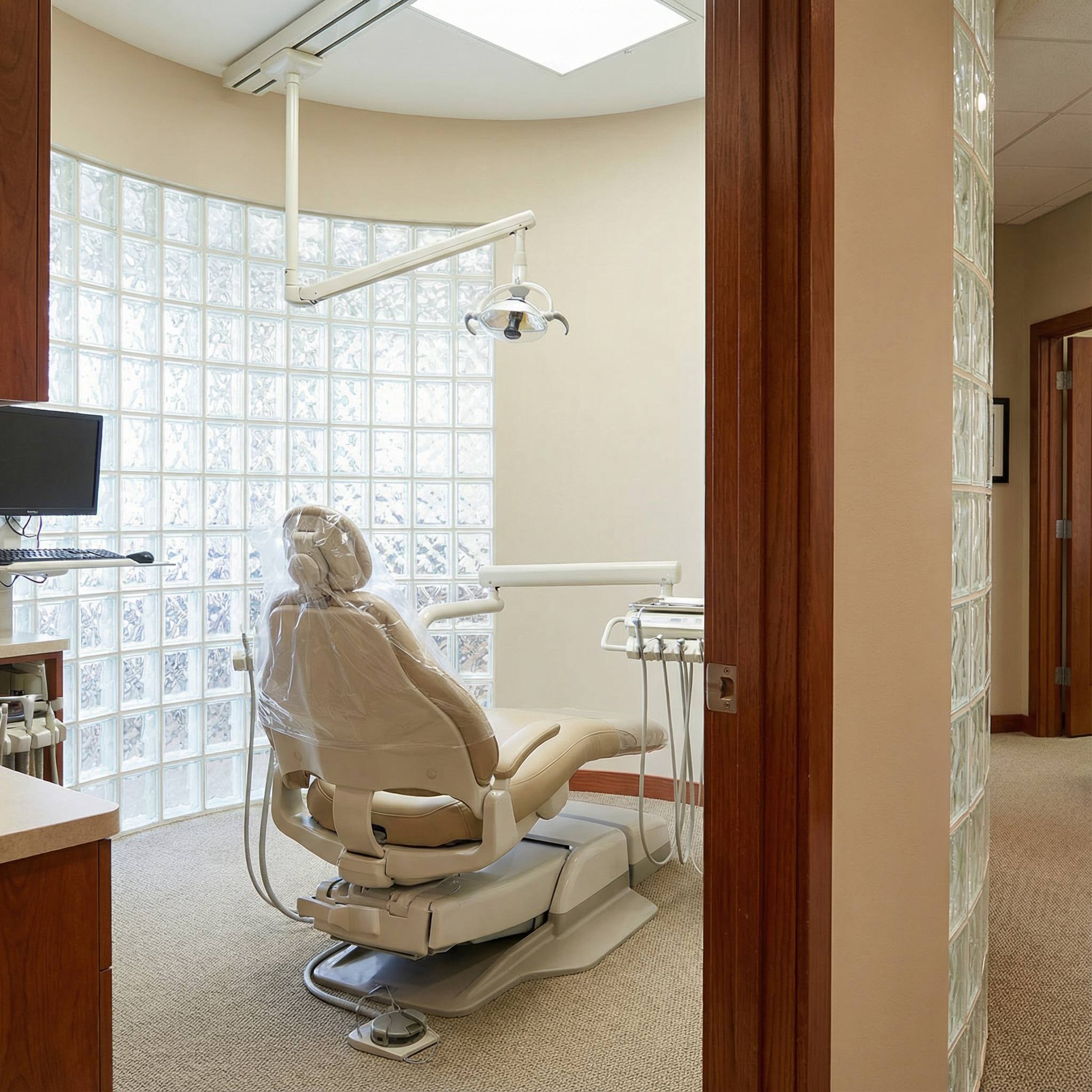 Treatment room with dental chair, glass block wall providing natural light, and modern equipment